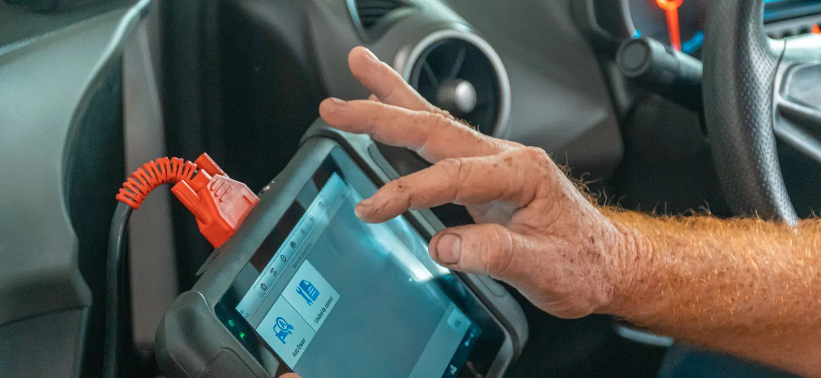 Technician's hand on a diagnostic scan tool plugged into a car's data port under the dashboard