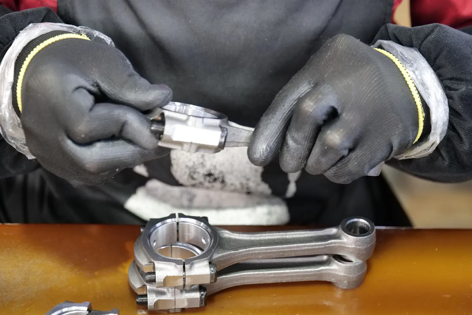 Technician holding a connecting rod over a bench with two more connecting rods and their bearing shells