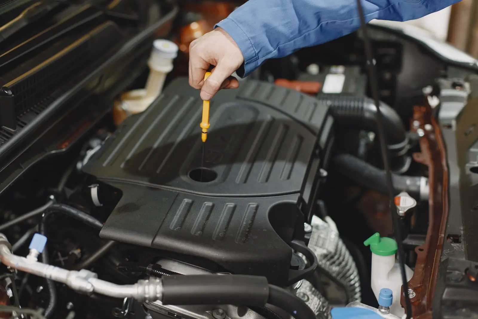 Hand pulling the yellow engine oil dipstick out of a car engine to check the oil level