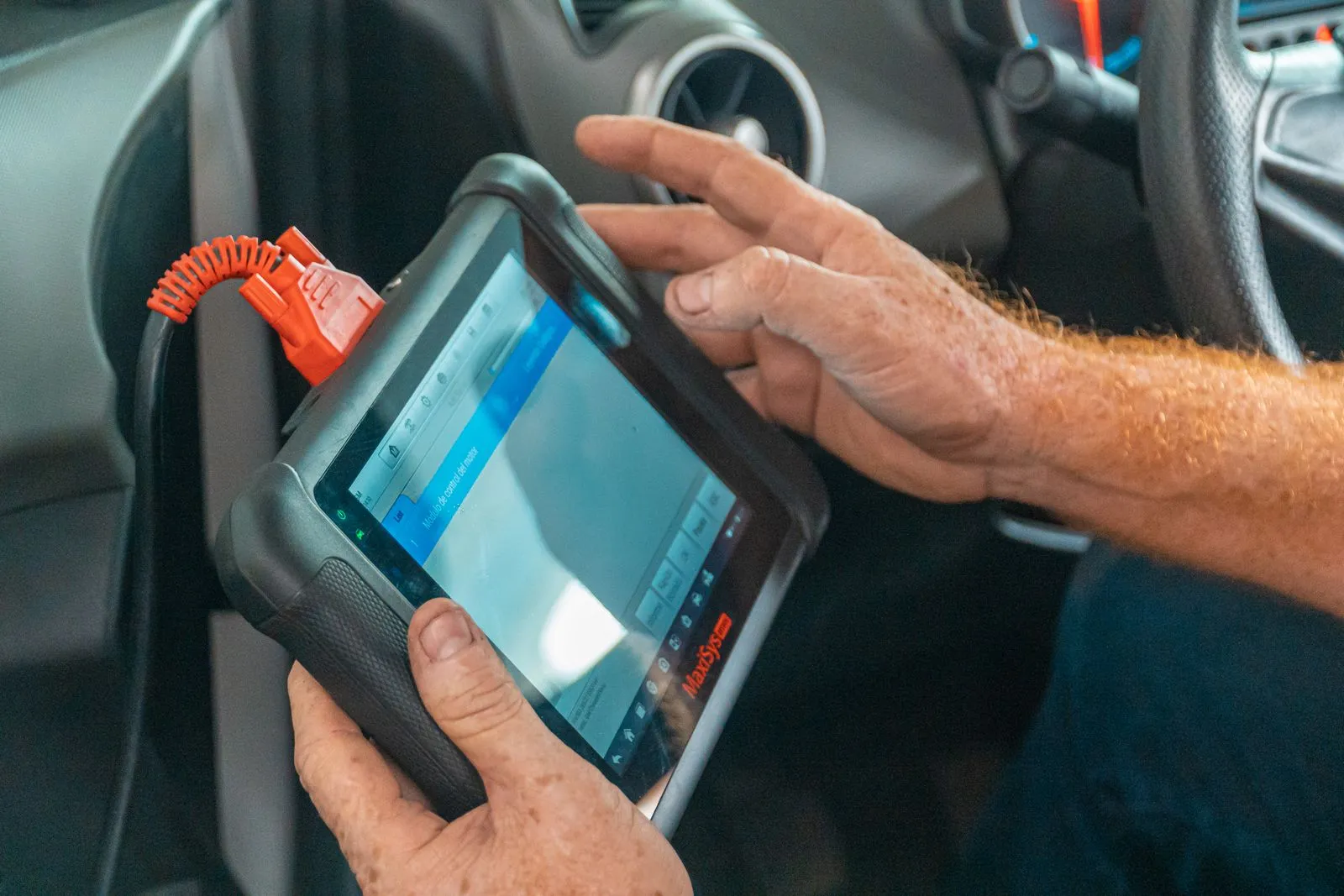 Mechanic holding a diagnostic scan tablet plugged into a car's data port, reading the control module screen from the driver's seat