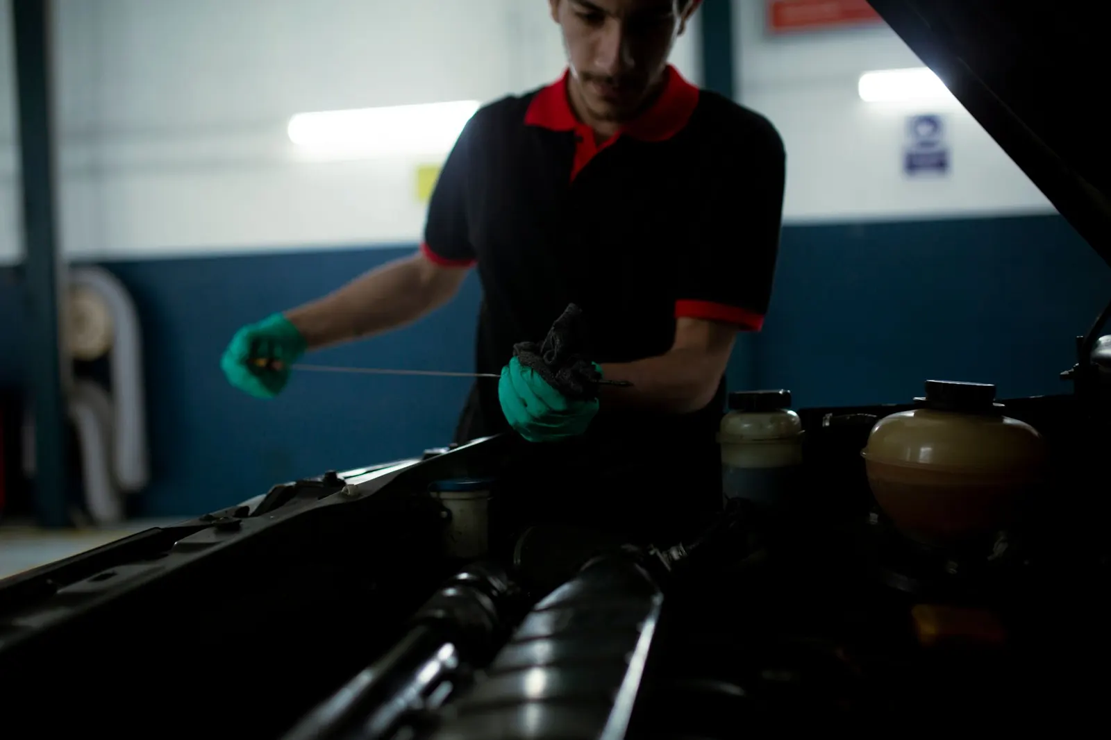 Mechanic in green gloves pulling the dipstick to check the engine oil level under an open hood in a repair shop